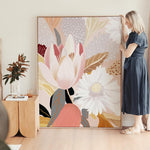 A woman standing next to a framed canvas print depicting a floral scene with soft, warm tones.