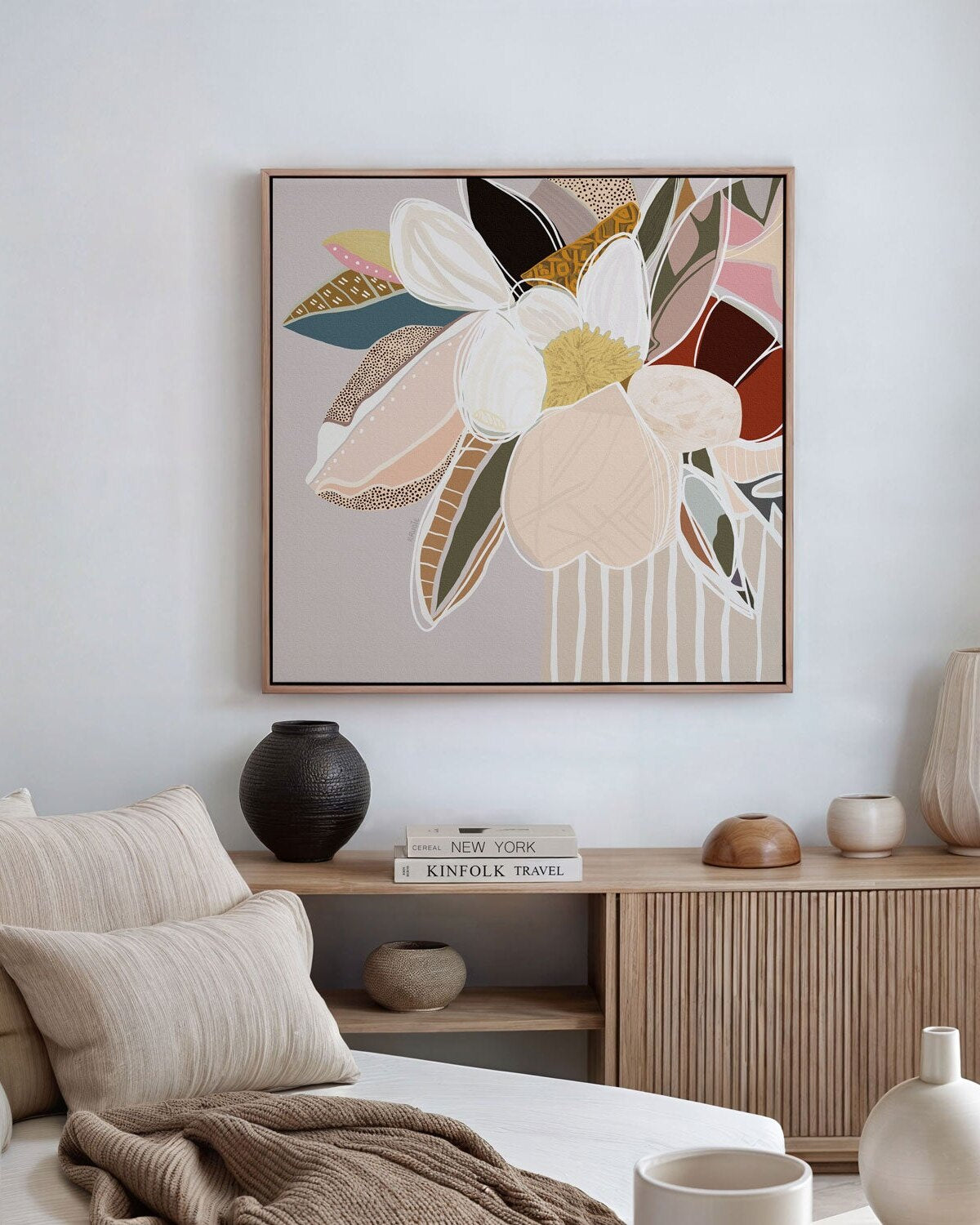 A framed canvas print featuring abstract florals in neutral colors displayed on a wall above a wooden side table with a framed picture, books, and decorative objects.