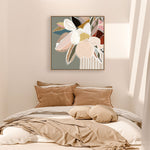 A framed canvas print with abstract florals in sage colors displayed above a bed with beige bedding and brown pillows.