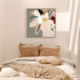 A framed canvas print with abstract florals in sage colors displayed above a bed with beige bedding and brown pillows.