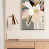 A framed canvas print titled 'Elodie In Sage No.2' hanging on a wall above a wooden cabinet, accompanied by a gold lamp with a white shade to the left.