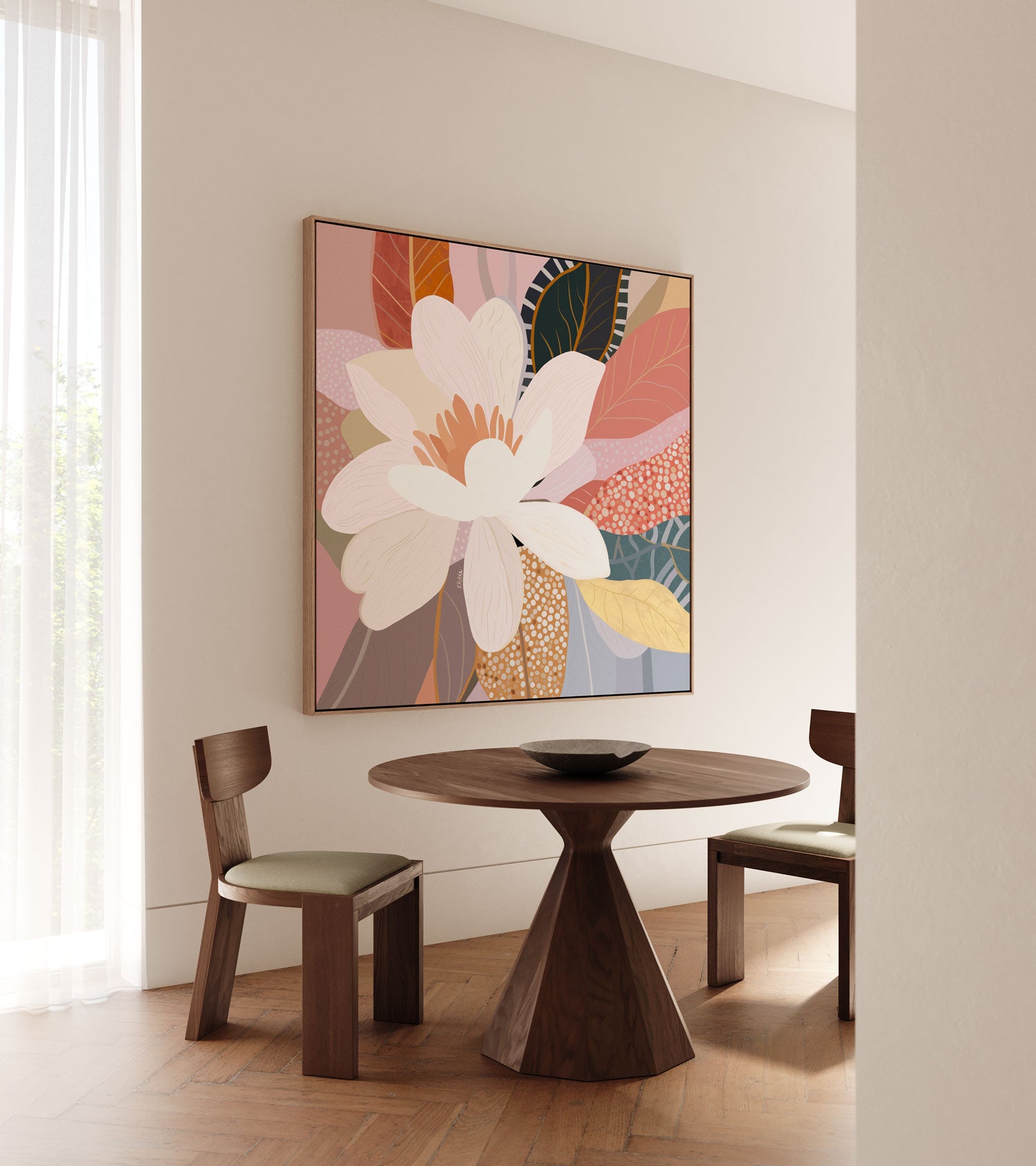 A framed canvas print titled 'Flourish', depicting a vibrant floral scene with a large flower in the center, displayed on a wall above a circular wooden table and flanked by two chairs.
