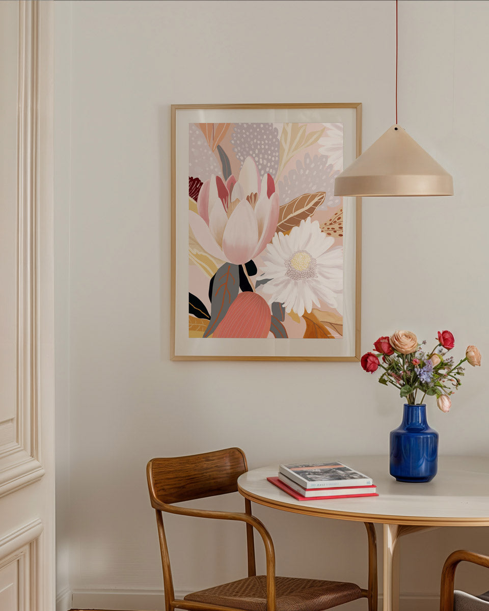 A framed abstract floral print hanging on a wall above a round table, with a chair and a pendant lamp in the room.