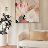 A framed canvas print featuring a serene spring motif, with a pastel color scheme, hanging on a wall above a white sofa, next to a wooden side table hosting a decorative vase.