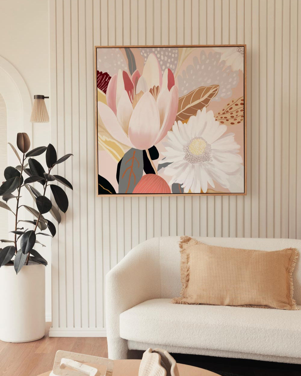 A framed canvas print featuring abstract floral art, displayed above a white sofa with gold cushions, in a room with striped wallpaper.