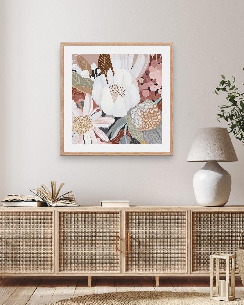 A framed print depicting Australian native flowers, displayed on a wall above a wooden cabinet with a lamp and plant beside it.