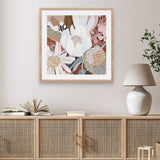 A framed print depicting Australian native flowers, displayed on a wall above a wooden cabinet with a lamp and plant beside it.