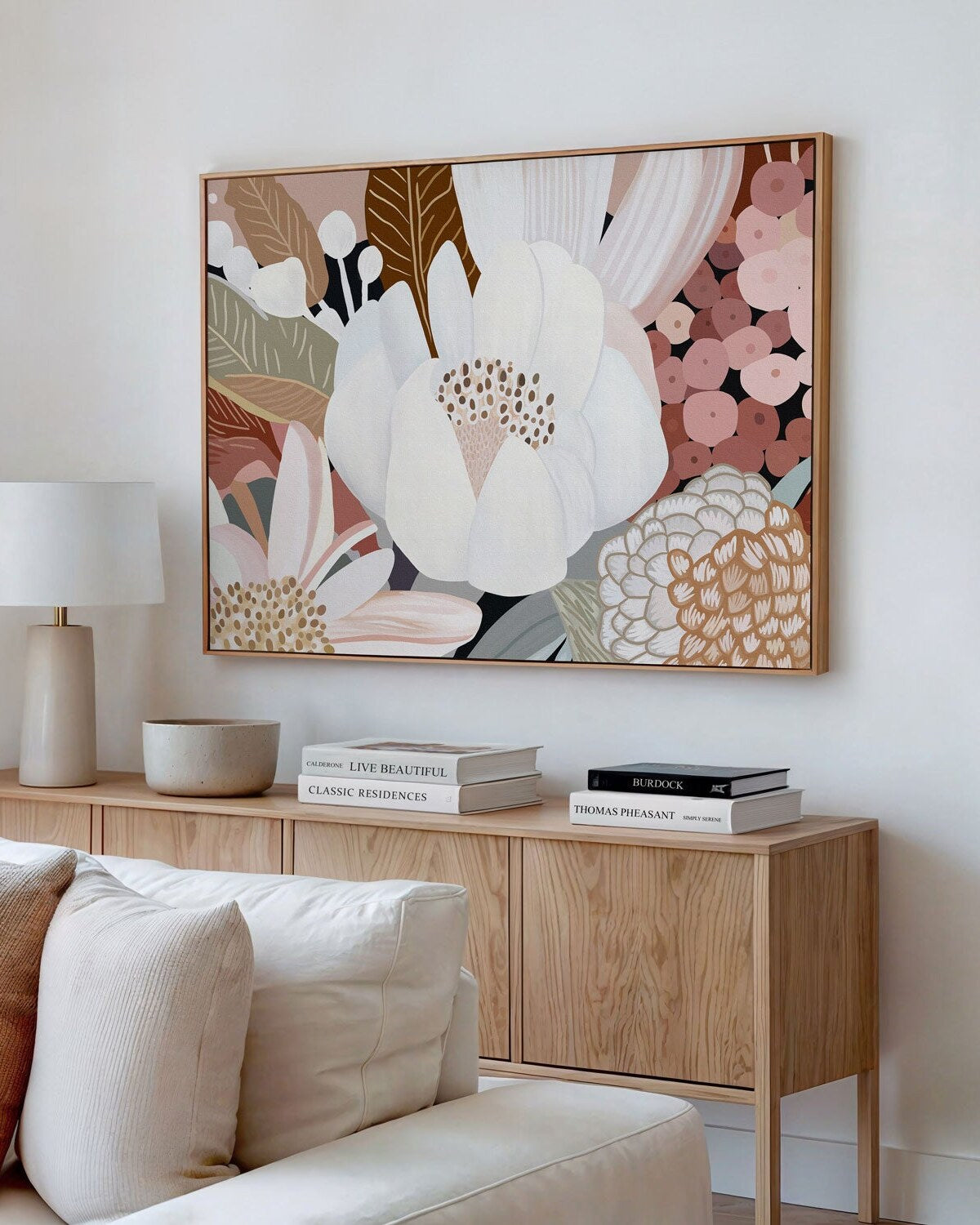 A framed canvas print titled 'Harmony No.3', featuring a floral composition in earthy tones, displayed above a wooden console table in a bright living room setting.
