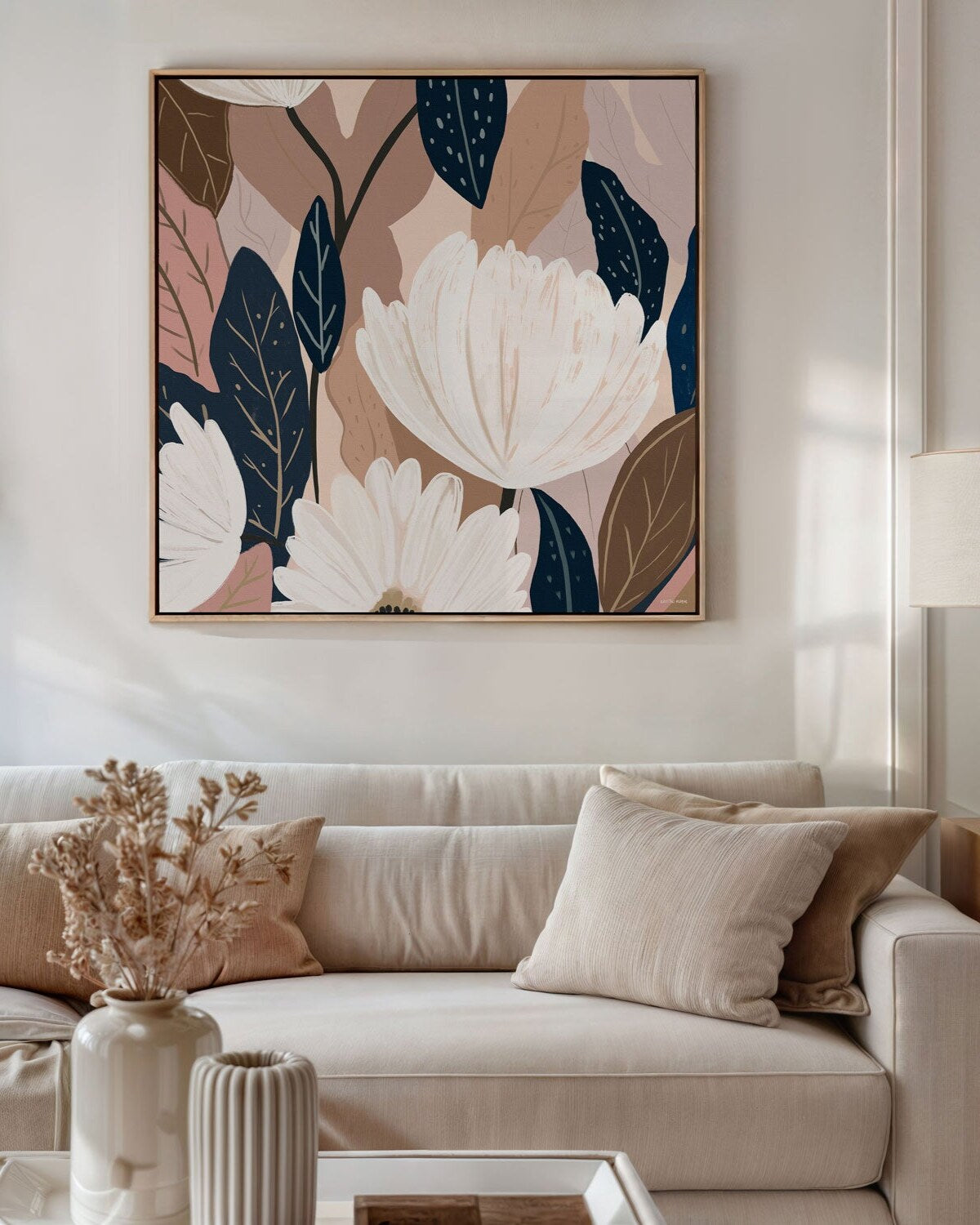 A framed canvas print titled 'Falling Into Place No.2', featuring a minimalist floral composition with soft pink, white, and green colors on a neutral background, displayed above a beige sofa with decorative pillows.