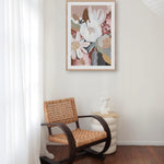 A framed print featuring a floral arrangement displayed above a vintage-style chair in a room with a light interior.
