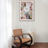 A framed print featuring a floral arrangement displayed above a vintage-style chair in a room with a light interior.