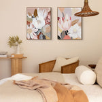 Two framed canvas artworks featuring abstract floral patterns, hung on a wall in a cozy room setting with a bed, chair, and lamp.