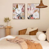 Two framed canvas artworks featuring abstract floral patterns, hung on a wall in a cozy room setting with a bed, chair, and lamp.