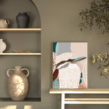 A framed canvas print titled 'Kookaburra in Pink No.2' displayed on a white wall, featuring an abstract depiction of a kookaburra with soft pink and beige tones.