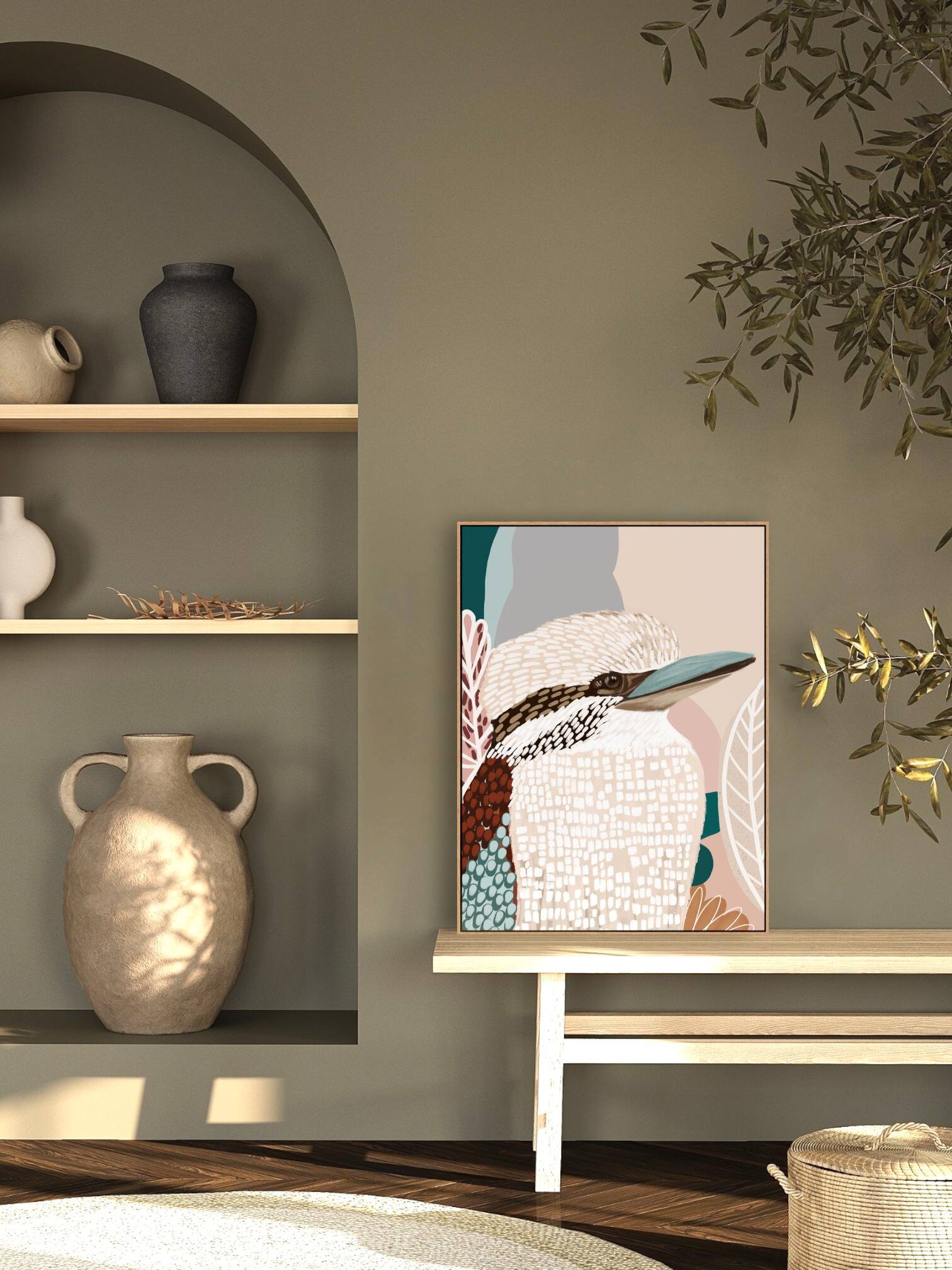A framed canvas print titled 'Kookaburra in Pink No.2' displayed on a white wall, featuring an abstract depiction of a kookaburra with soft pink and beige tones.