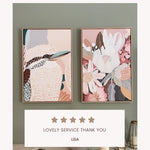 A framed canvas print titled 'Kookaburra in Pink No.2' displayed on a white wall, featuring an abstract depiction of a kookaburra with soft pink and beige tones.