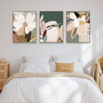 A set of three framed canvas prints featuring floral artwork, displayed above a bed in a cozy interior setting.