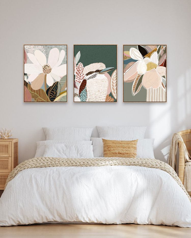 A set of three framed canvas prints featuring floral artwork, displayed above a bed in a cozy interior setting.