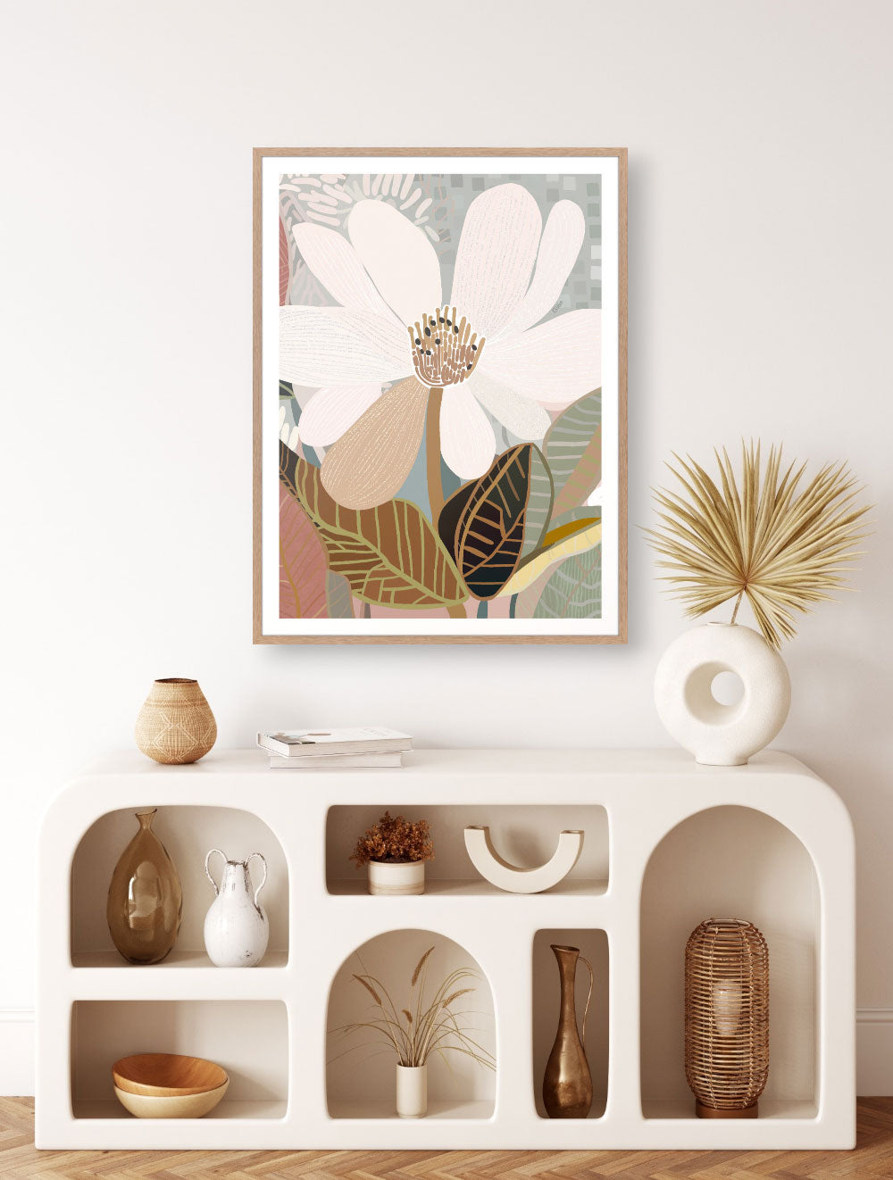 A framed print of an abstract floral artwork featuring a magnolia flower on a white wall, with decorative items arranged on a white shelf below.