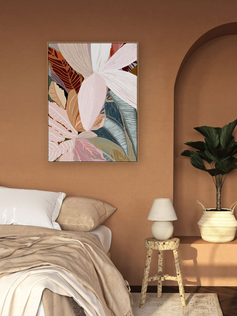 A framed canvas print of abstract palm leaves displayed on a wall in a room with a bed and lamp.