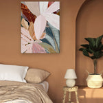 A framed canvas print of abstract palm leaves displayed on a wall in a room with a bed and lamp.