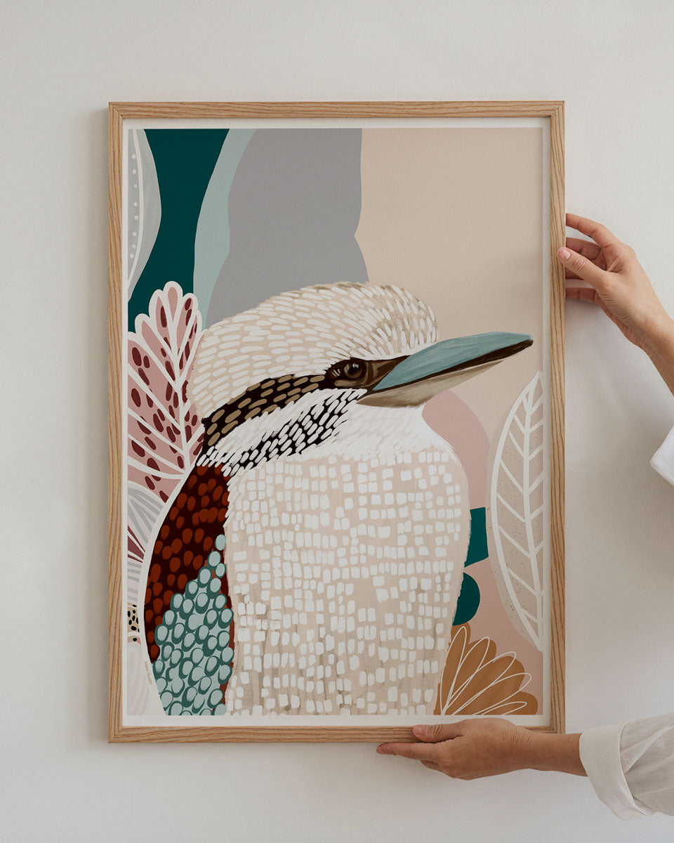 Framed artwork of a kookaburra with abstract patterns held by a person against a white wall.