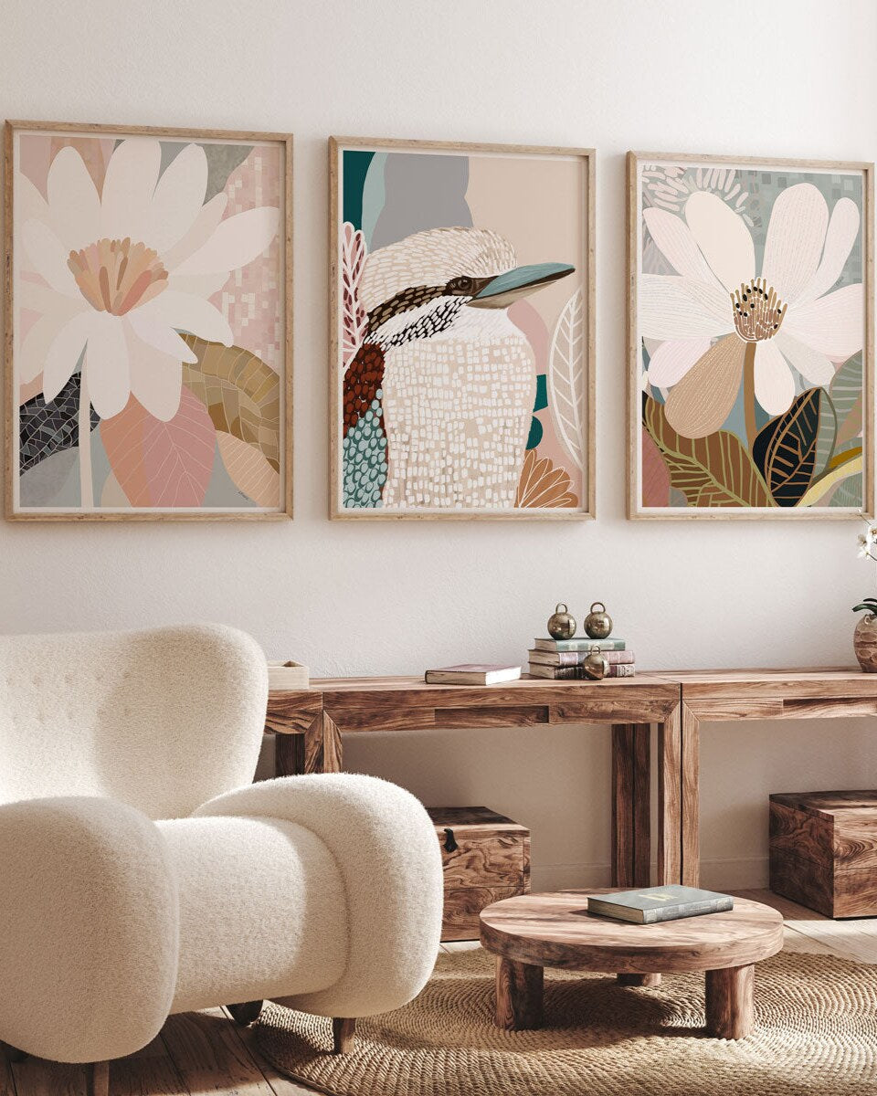 A set of three framed art prints featuring abstract floral designs, displayed in a living room setting with a modern armchair and wooden furniture.