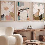 A set of three framed art prints featuring abstract floral designs, displayed in a living room setting with a modern armchair and wooden furniture.