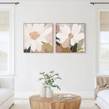 A pair of framed canvas prints titled 'Reverie No.2' and 'Magnolia' displayed in a living room setting with a natural oak frame and a classic black moulding, respectively.