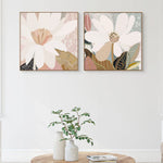 Two framed canvas prints with floral artwork hanging on a wall above a wooden table.