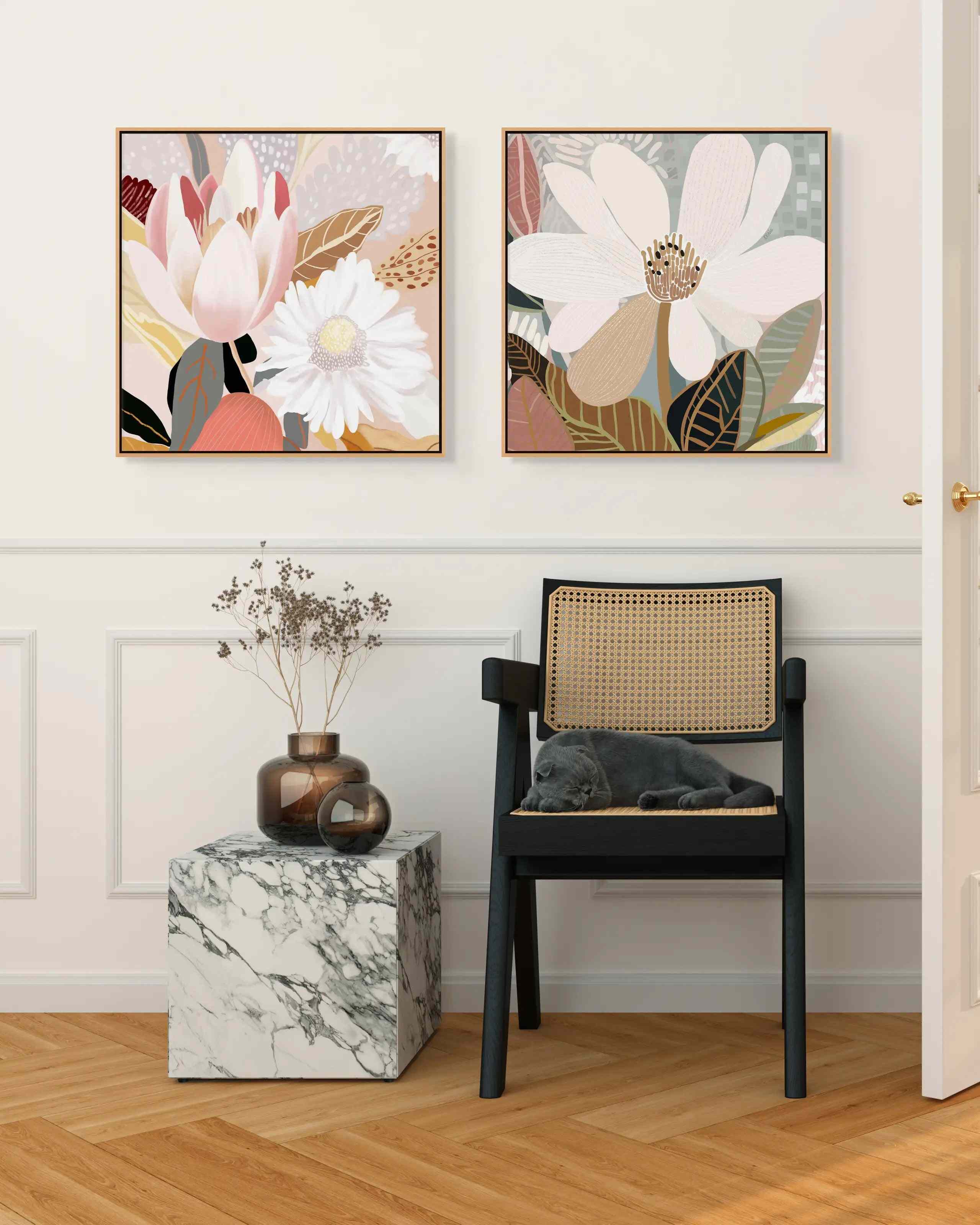 Two framed canvas prints featuring floral artwork, hanging on a wall above a small marble-topped side table and a black chair.