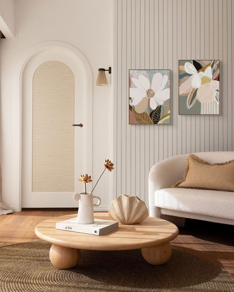 A framed canvas art piece with floral print hanging on a wall above a white sofa, with a round wooden coffee table in the foreground featuring a book and a vase with flowers.