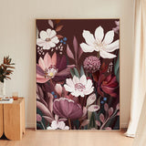 A large framed botanical art print featuring white and pink flowers with deep purple and burgundy tones, leaning against a beige wall in a modern room with light wood flooring.