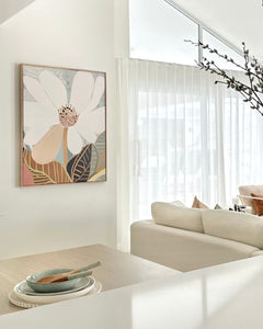A framed canvas print of an abstract floral artwork featuring a magnolia flower, displayed on a wall above a modern sofa in a well-lit living room.