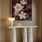Marble console table with decorative items against a beige wall with floral artwork.