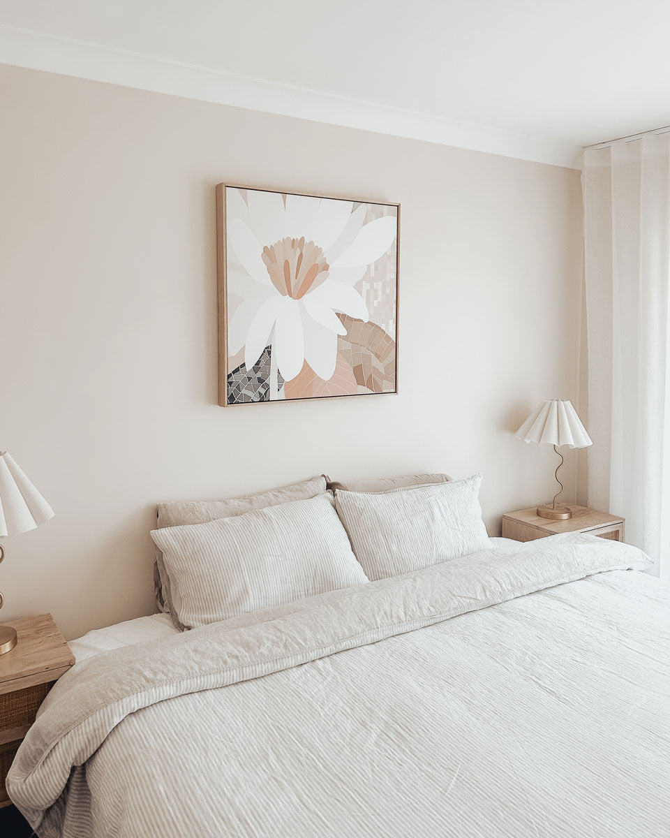 Neatly made bed in a bedroom with abstract wall art and lamps.