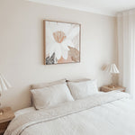 Neatly made bed in a bedroom with abstract wall art and lamps.