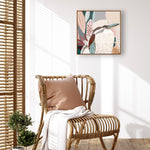 Framed canvas print of a Kookaburra perched on a branch with pink blossoms in the background, displayed above a rattan chair with a white cushion and a small potted plant.